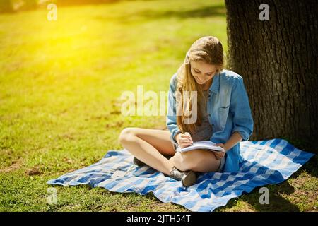 In der Natur zu sein inspiriert die Kreativität. Ein junger Student studiert unter einem Baum im Park. Stockfoto