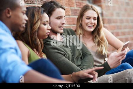 Es wird immer einfacher, in diesen Tagen zu verbinden. Eine Gruppe von jungen Freunden mit einem Mobiltelefon zusammen. Stockfoto