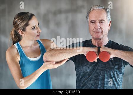 Älter werden und gesünder werden. Ein älterer Mann, der Gewichte mit Hilfe eines Physiotherapeuten verwendet. Stockfoto