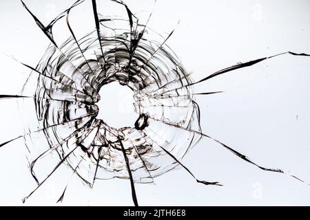 Risse im Glas, ein Loch aus Kugeln im Glas auf weißem Hintergrund. Glasstruktur des Fensters. Stockfoto