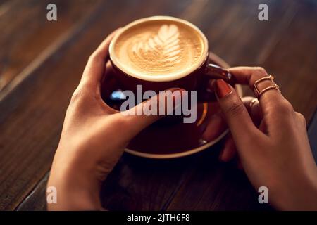 Umarmung in einem Becher. Nahaufnahme einer nicht identifizierbaren Frau, die eine Tasse Kaffee in einem Café genießt. Stockfoto