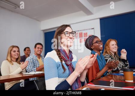 Fühlen Sie sich motiviert nach einem inspirierenden Gespräch von ihrem Dozenten. Eine Gruppe von Studenten applaudieren zusammen in der Klasse. Stockfoto