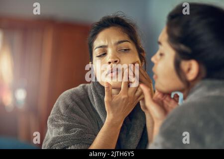 Ist das ein Fleck, den ich sehe. Eine junge Frau runzelte die Stirn, während sie eine Unvollkommenheit auf ihrer Haut im Spiegel untersuchte. Stockfoto