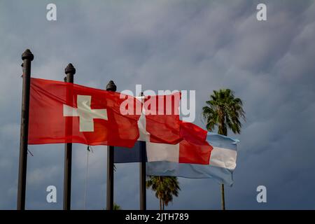 Flaggen der Schweiz, Italiens, Frankreichs und Argentiniens flattern unter stürmischem Himmel im Wind. Stockfoto