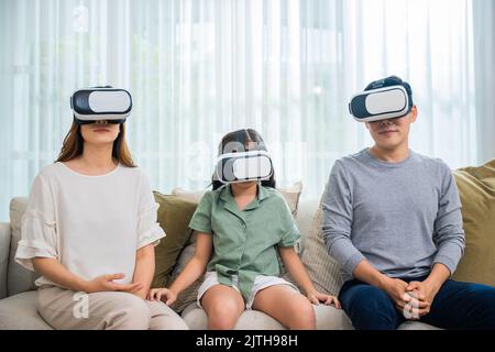 Glückliche Familie haben Mutter Vater und Tochter Film ansehen oder Videospiel spielen, asiatische Familie tragen vr Brille Kopfhörer Spaß sitzen auf dem Sofa im Leben Stockfoto