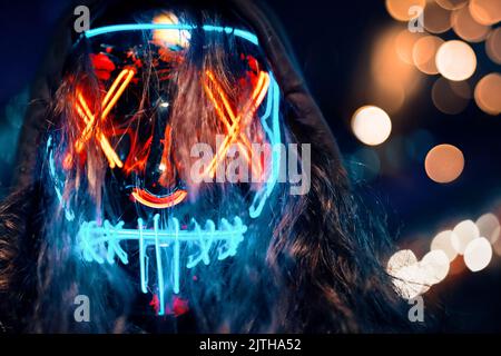 Mann im Hoodie mit langen zerzaust Haaren in einer leuchtenden neon leuchtenden Maske. Stockfoto