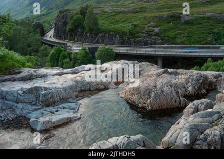 Die untergehende Sonne, über dem dramatischen Tal von Glen Coe, im Sommer, wo sich drei kleine Flüsse treffen, am Fuße der Three Sisters of Glen Coe, mit AW Stockfoto