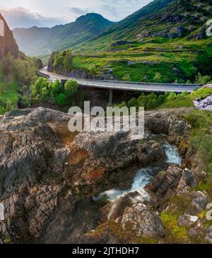 Die untergehende Sonne, über dem dramatischen Tal von Glen Coe, im Sommer, wo sich drei kleine Flüsse treffen, am Fuße der Three Sisters of Glen Coe, mit AW Stockfoto