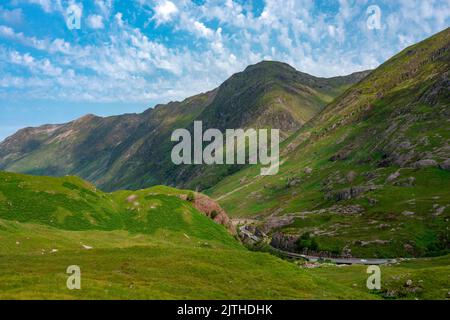 Schön, Bereich der Highlands, bedeckt mit grünem Sommerrasen, blauer Himmel oben. Die Straße schlängelt sich zwischen der herrlichen Landschaft, beliebt bei Touristen, hallo Stockfoto