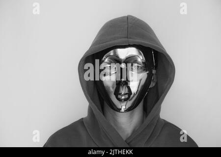 Ein Mädchen in einer Vollmaske aus Kunststoff und in einer Kapuze auf einem isolierten Hintergrund, Anonymität, versteckt ihr Gesicht Stockfoto