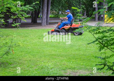 Benzin-Rasenmäher. Fahren Benzin Rasenmäher Maschine im Freien im Park. Einsatz von Technologie in der Gartenbaugrundpflege. Seitenansicht des Arbeiter-Drivi Stockfoto