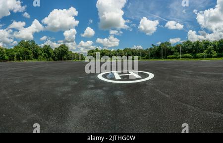 Asphalt-Hubschrauberlandeplatz im Wald. Landschaft des Hubschrauberlandeplatz. Hubschrauberlandeplatz vor blauem Himmel und weißen Cumuluswolken an sonnigen Tagen. Plattform für Hubschrauber Stockfoto