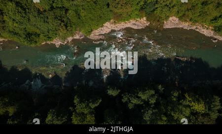 Smaragdgrüner Fluss mit steinerner Küste und Wald, starker Bach mit Wendungen von kristallklarem Bergfluss. Luftdrohne im Sommer von oben nach unten Stockfoto
