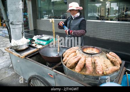 Street Food, geröstete Süßkartoffeln und Kastanien, die in einem Wok gebraten werden, der von einem chinesischen Verkäufer verkauft wird. Stockfoto