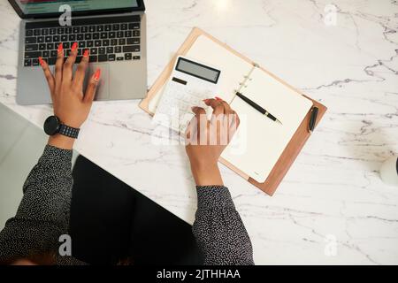 Hände einer Geschäftsfrau, die am Jahresbericht arbeitet, Berechnungen durchführt und sich im Planer Notizen macht Stockfoto