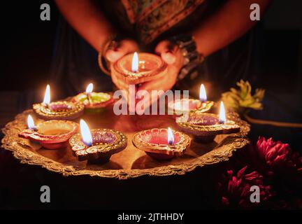 Diwali, Deepavali Hindu Festival der Lichter Feier. Diya Öllampe in Frauenhänden beleuchtet, dunkler Hintergrund. Nahaufnahme. Stockfoto