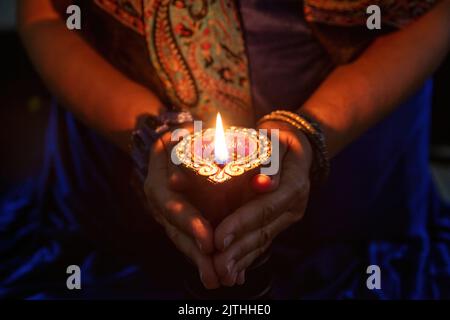 Diwali, Deepavali Hindu Festival der Lichter Feier. Diya Öllampe in Frauenhänden beleuchtet, dunkler Hintergrund. Nahaufnahme. Stockfoto