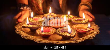 Diwali. Frau, die ein Tablett mit angezündeten Diya-Öllampen in der Hand hält, Deepavali-Feier. Hindu Festival der Lichter im Freien, Indien Straßen. Stockfoto