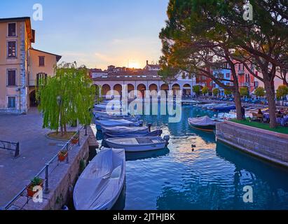 Der Sonnenuntergang über dem Porto Vecchio (Alter Hafen) mit kleinen Häusern und Fischerbooten, Desenzano del Garda, Gardasee, Italien Stockfoto