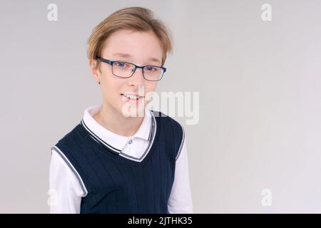 Zuckender kaukasischer Junge, zweifelende zuckende Schultern, Schuljunge, Teenager mit Brille in einem weißen T-Shirt. Der Junge wählt auf einem grauen Hintergrund. Stockfoto