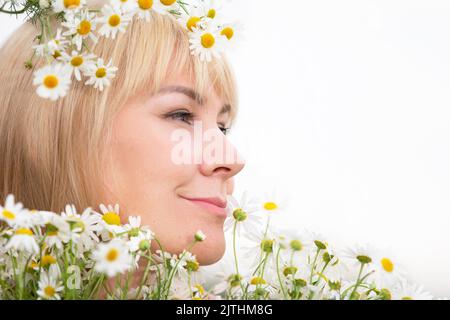 Das Gesicht einer prallen blonden Frau mittleren Alters im Profil vor einem Hintergrund von Gänseblümchen. Stockfoto