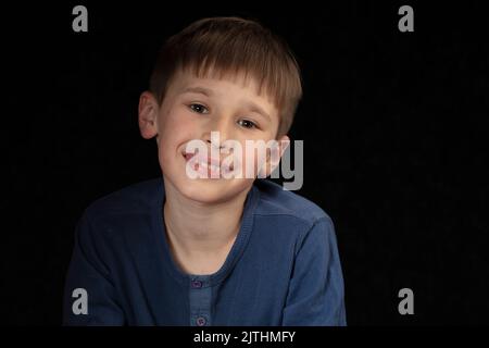 Porträt eines zehnjährigen Jungen auf dunklem Hintergrund. Das Kind blickt mit intelligenten Augen in die Kamera. Hübscher Junge im Schulalter. Stockfoto