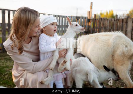 Mama mit einer kleinen Tochter füttert eine Ziege. Eine Frau mit einem Kind auf einem Bauernhof. Stockfoto