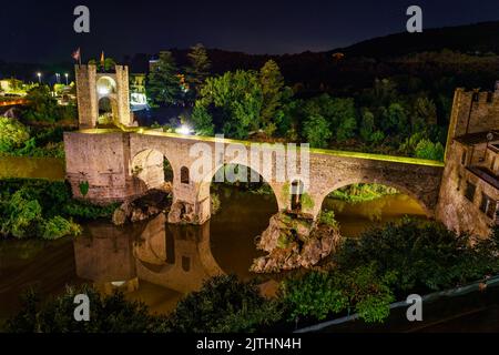 Römische Brücke, die den Fluss überquert und den Zugang zur malerischen Stadt Besalu bei Nacht, Girona, Katalonien, ermöglicht. Stockfoto