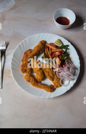Draufsicht auf gebratene Hähnchenflügel zusammen mit Gewürzen auf einem weißen Teller. Stockfoto