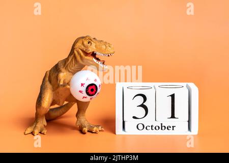 Spielzeug-Dinosaurier Tyrannosaurus mit Auge in den Pfoten, Kalenderdatum 31 Oktober isoliert auf orangefarbenem Hintergrund Feiertag Grußkarte Happy Halloween day c Stockfoto