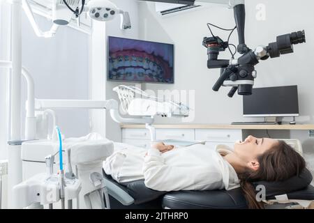 Mit dem Zahnmikroskop Behandlung der Zähne des Patienten in der Zahnarztpraxis. Medizin, Zahnmedizin und Gesundheitswesen Konzept. Zahnärztliche Ausrüstung Stockfoto
