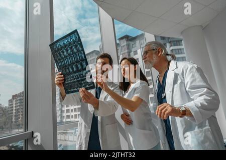 Arztkollegen schauen sich die Röntgen- oder MRT-Untersuchung der Wirbelsäule des Patienten in der Medizinklinik an und diskutieren sie Stockfoto