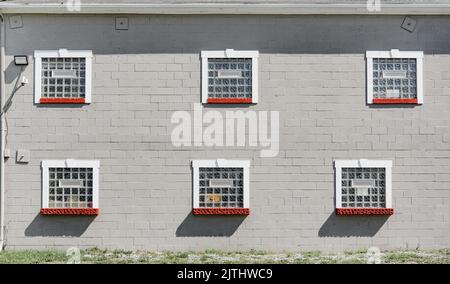 Ein normales Gebäude mit weißen Ziegeln und sechs quadratischen Fenstern an einem sonnigen Tag Stockfoto