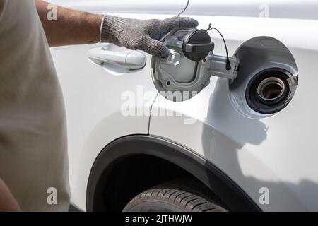 Der Mann öffnet die Luke des Gastanks des Autos. Mit Handschuhen geriebte Hand öffnet den Gastank Stockfoto