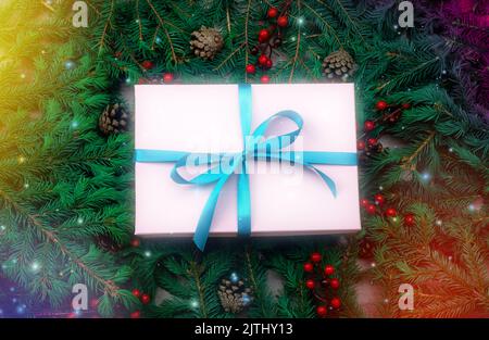 weihnachtsgeschenk, rosa Box mit Band liegt auf dunklen Fichtenzweigen. Bunte weihnachtslichter leuchten. Geschenkschachtel aus rosa Papier, blauem Band und eingewickelt Stockfoto