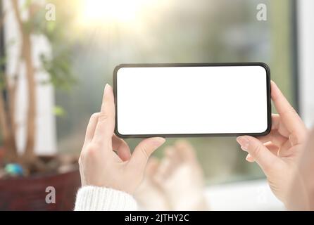 Handy-Modell. Frau schaut sich Videoinhalte auf dem Mobiltelefon oder Smartphone mit weißem leeren Bildschirm an. Telefon horizontal halten Stockfoto