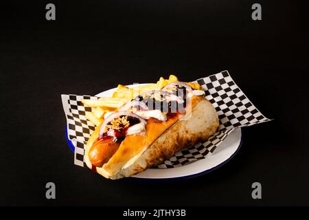 Frankfurter Wurst mit Zwiebel, Käse und pommes auf einem weißen Teller auf schwarzem Hintergrund Stockfoto