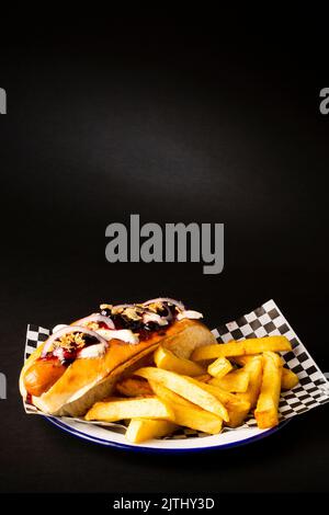 Frankfurter Wurst mit Zwiebel, Käse und pommes auf einem weißen Teller auf schwarzem Hintergrund Stockfoto