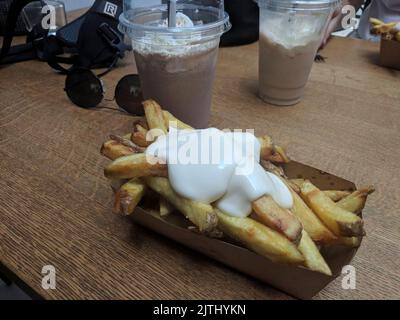 Karton mit Pommes Frites, bedeckt mit Mayonnaise, Eiskaffee und Schlagsahne auf einem Tisch vor einem Restaurant in Den Haag, Niederlande Stockfoto
