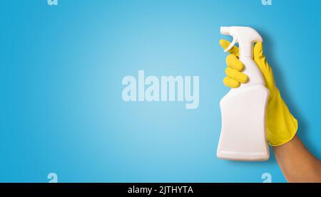 Hand in gelben Gummi-Handschuh hält weißen blanken Reinigungsspray-Flasche auf blauem Hintergrund. Copy Space Stockfoto