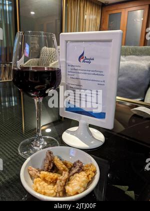 Ein Glas Rotwein und eine Schüssel Snacks auf einem Tisch in der Bangkok Airways Business Lounge des Bangkok International Airport, Thailand Stockfoto