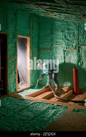 Männlich Baumeister isolierenden Holzrahmen Haus. Mann Arbeiter sprühen Polyurethan-Schaum in der zukünftigen Hütte, mit Plural Komponente Pistole. Bau- und Isolierkonzept. Stockfoto