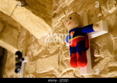 Gestrickte Superman und Batman auf weißen Holzkreuzen im Rahmen einer Kunstausstellung in Mdina, Malta. Stockfoto