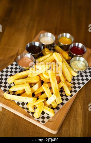 Pommes frites auf einem Holztisch, begleitet von verschiedenen Saucen auf einem Holztisch Stockfoto