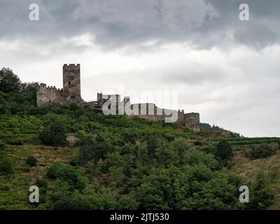 SPITZ, ÖSTERREICH - 13. JULI 2019: Die Ruinen von Schloss Hinterhaus auf den bewaldeten Hügeln über der Stadt Stockfoto