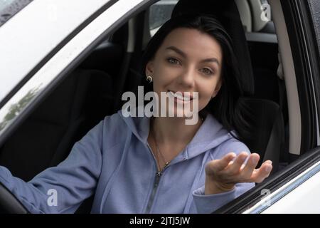 Eine lächelnde junge Frau sitzt in ihrem Auto und lächelt. Eine Frau spricht mit jemandem durch das Fenster ihres Autos. Stockfoto