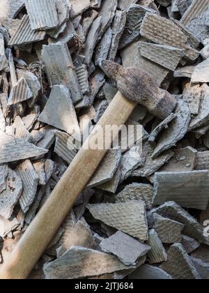 Ein alter Hammer liegt auf alten Schieferstücken. Ein Hammer vor dem Hintergrund von zufällig verstreuten Teilen von zerbrochenem Asbest. Stockfoto