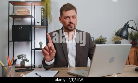 Geschäftsmann im Anzug, der am Laptop arbeitet, schüttelt den Finger und sagt nein, sei vorsichtig, schimpfend und gibt Ratschläge, um Gefährdungsfehler zu vermeiden, Abzeichnung im Büro. Selbstbewusster, seriöser Freiberufler Stockfoto