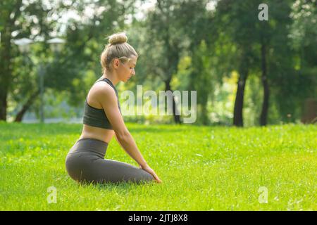 Schlanke Frau, die in Sportkleidung auf dem grünen Gras im Park sitzt Stockfoto