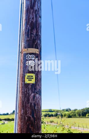 Schild an einem hölzernen Telefonmast, der die Personen darauf hinweist, dass der Mast Glasfaserkabel trägt. Stockfoto